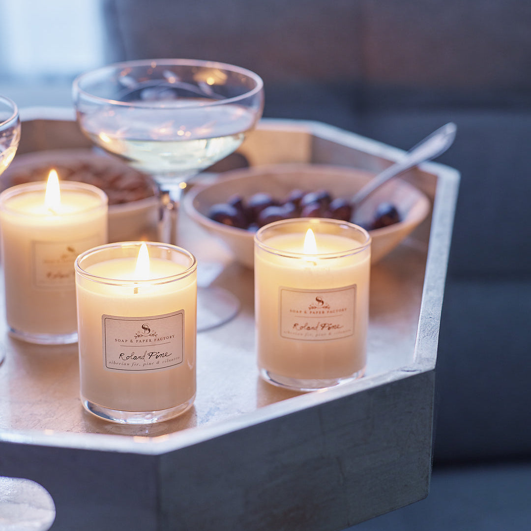 Roland Pine Votive  lit candles on a tray with a glass of water and a bowl on a tray. 