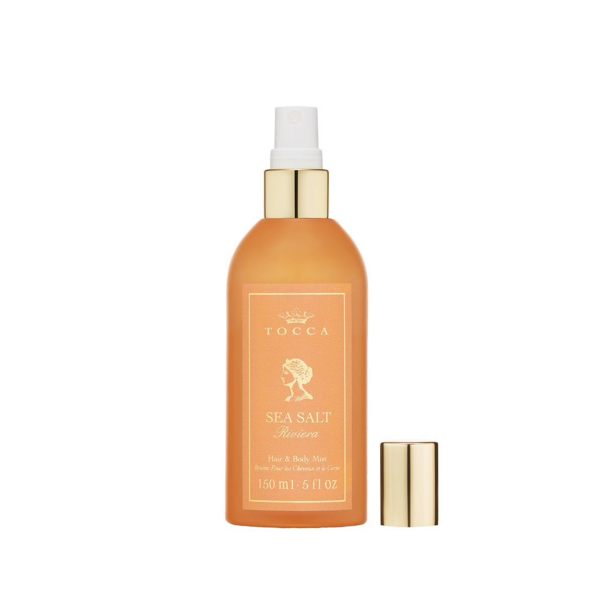 A bottle of TOCCA Sea Salt Riviera - Hair and Body Mist in an amber-orange spray bottle with gold accents, shown with its cap off next to it on a white background.