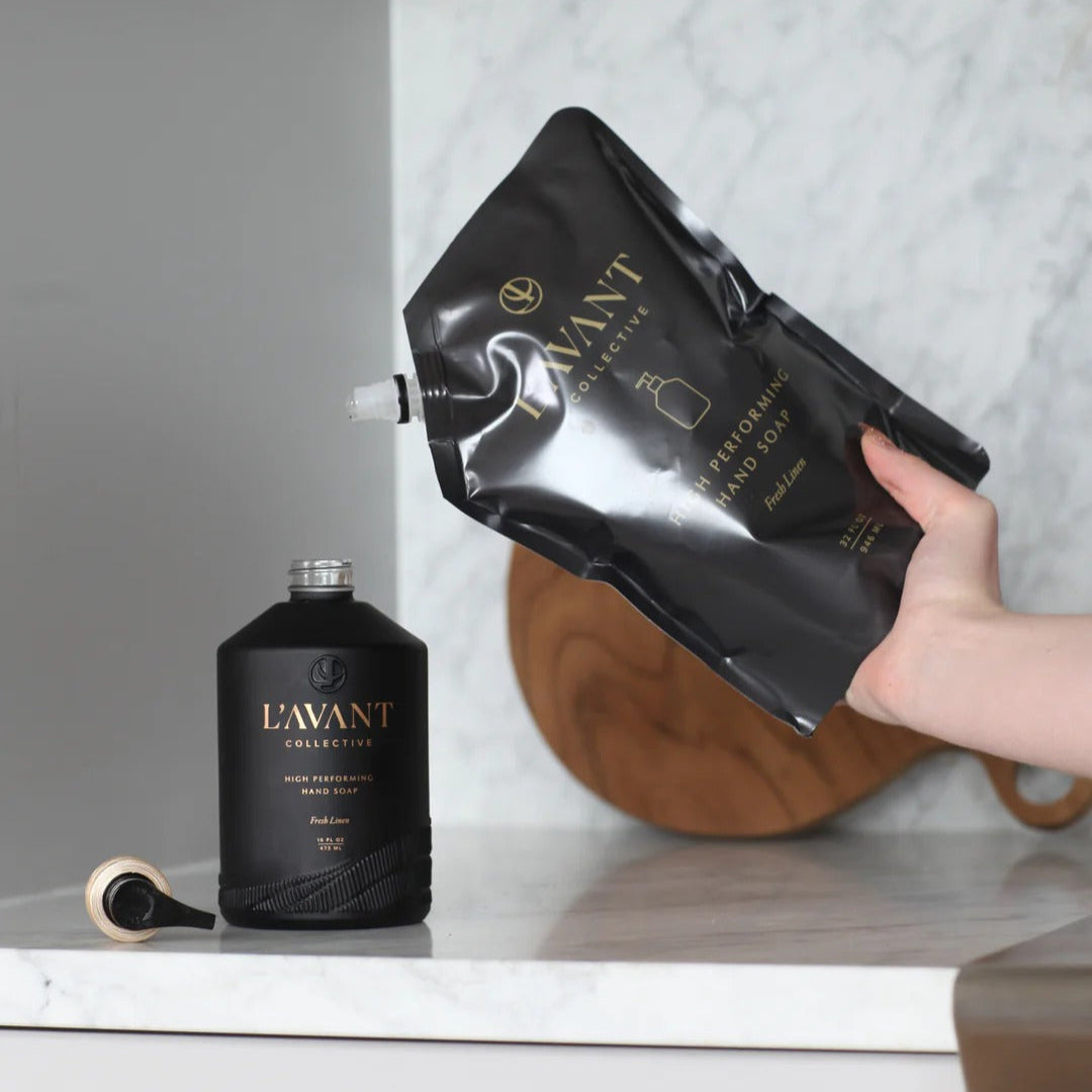 Person holding a black pouch labeled 'L'AVANT' next to a black bottle on a marble surface.