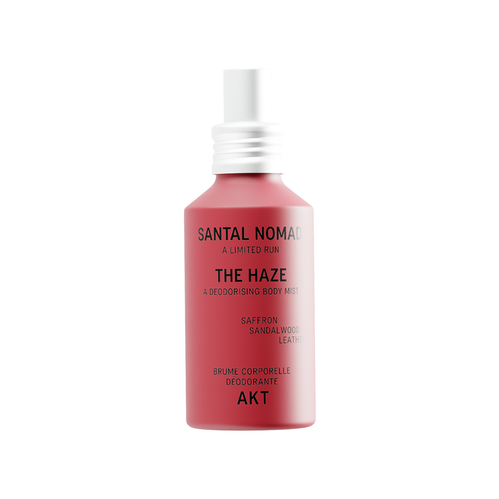 A red spray bottle of The Haze - Santal Nomad - Limited Edition deodorizing body spray, featuring a white spray nozzle and silver collar, on a solid white background.