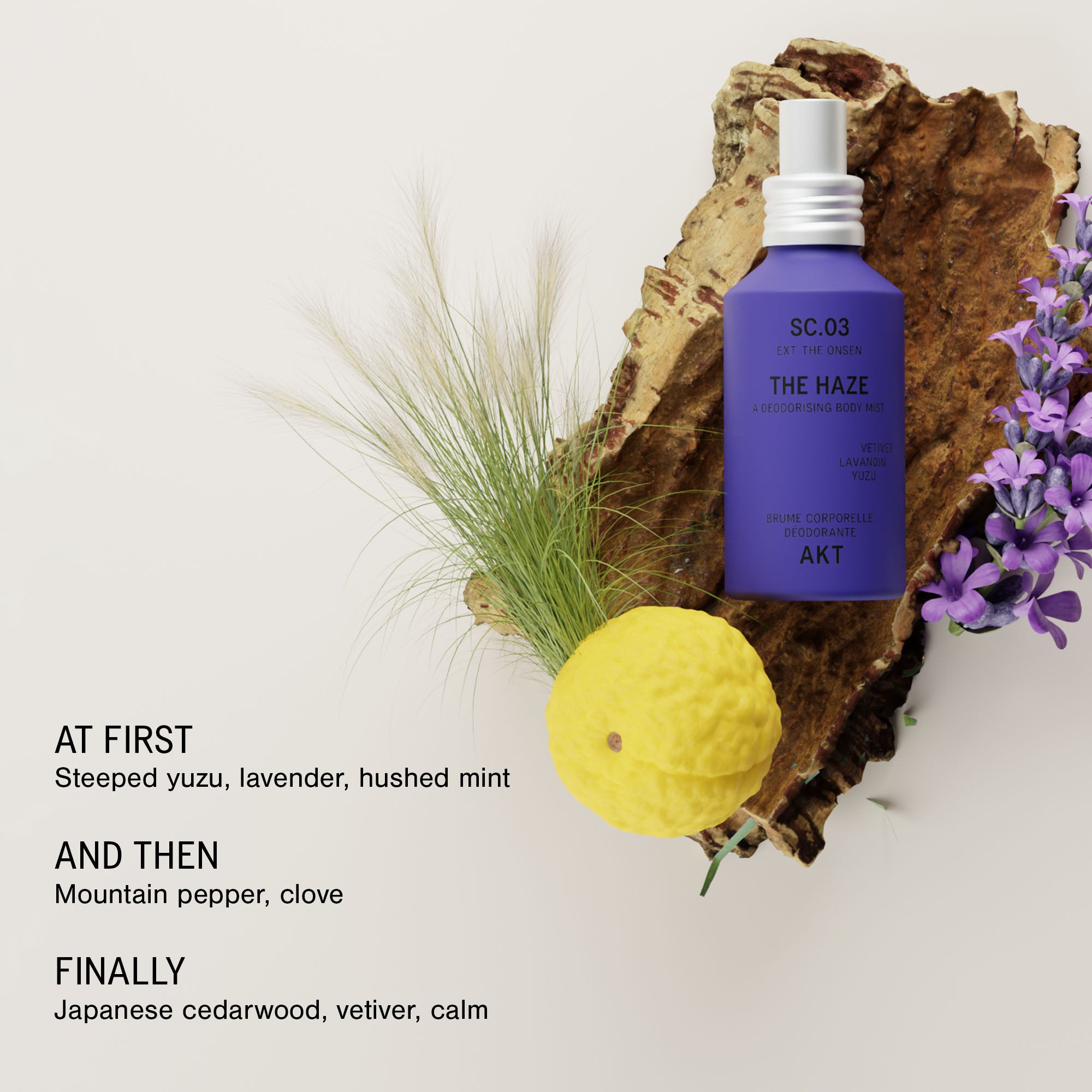 Bottle of AKT The Haze SC. 03 The Onsen styled on a piece of bark with dried grass, a yellow citrus fruit, and purple flowers on a light background, with scent notes listed on the left.