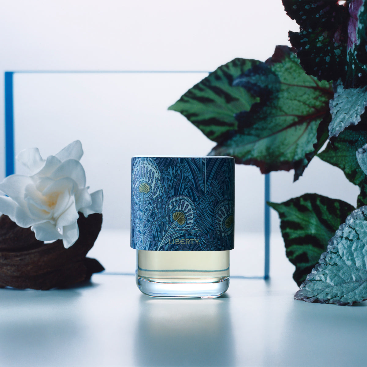 Glass with blue decorative label next to white flowers and green leaves on a light background