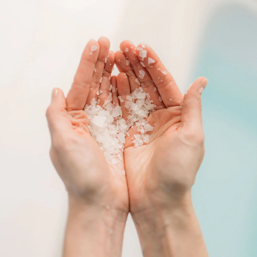 Two hands holding small hinoki bath flakes against a blurred background