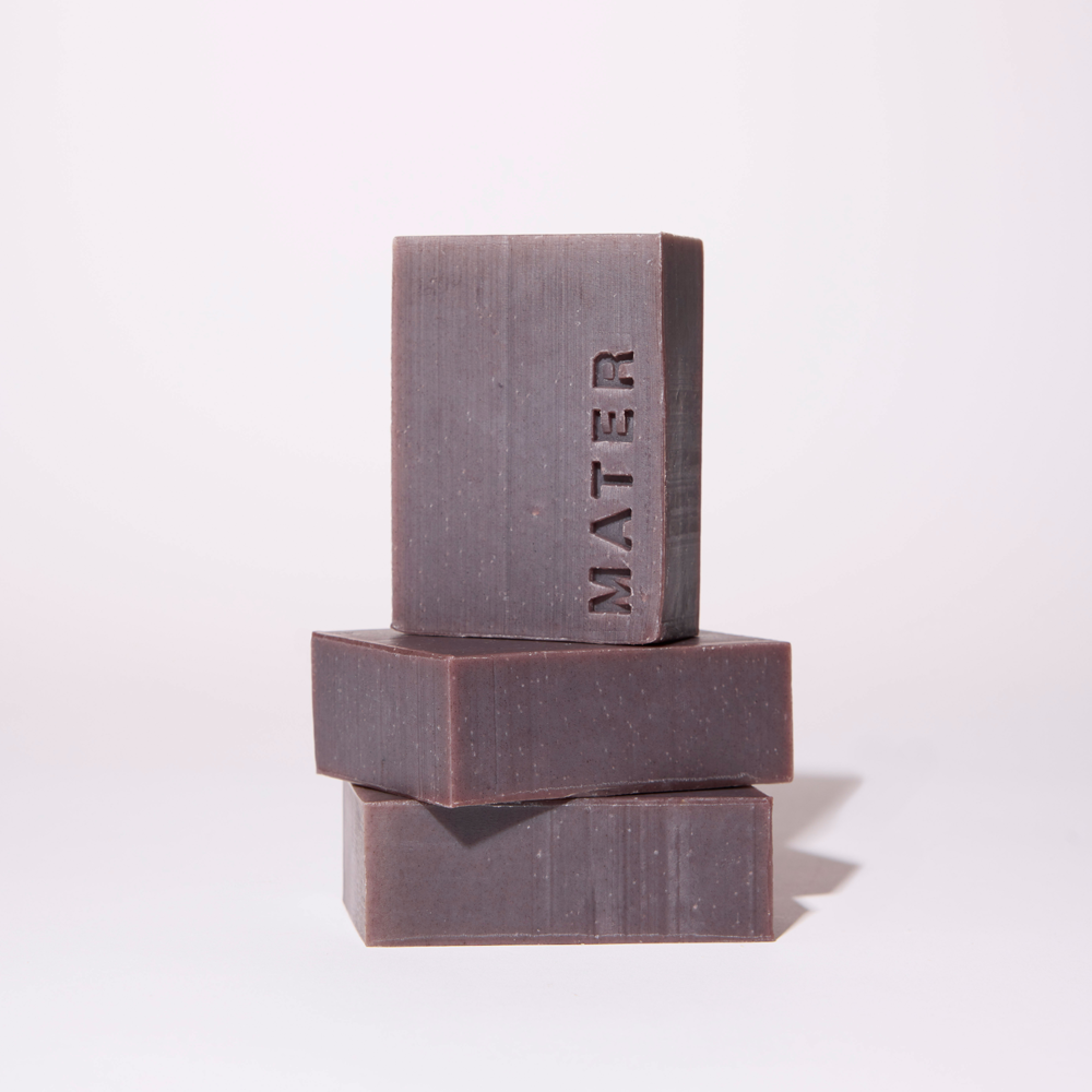 Three stacked rectangular bars of MATER soap in a dark charcoal gray color, photographed on a clean white background.