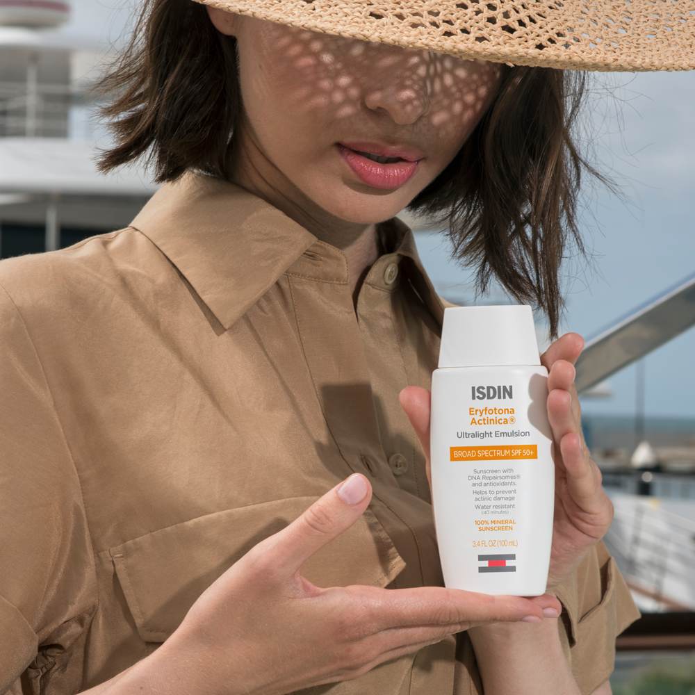 Woman in coastal scene holding a bottle ISDIN Eryfotona Actinica SPF 50+