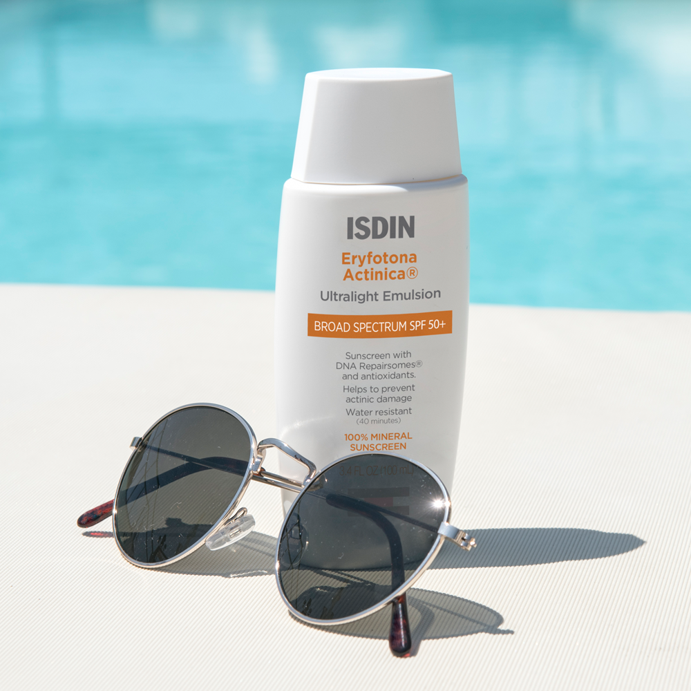 ISDIN Eryfotona Actinica SPF 50+ bottle with sunglasses next to a pool