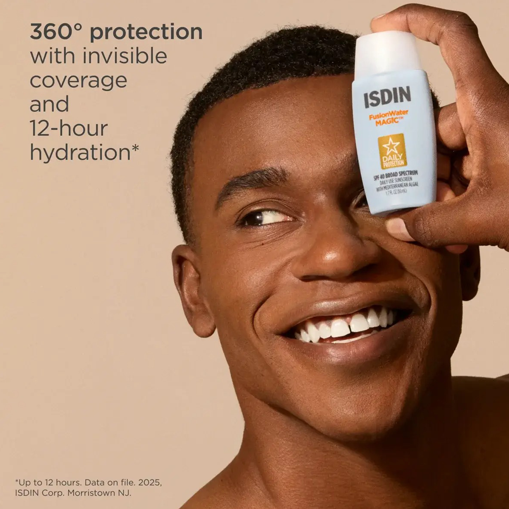 A smiling man holds an ISDIN Powerhouse Magic SPF 50 sunscreen bottle against his eye, with promotional text on a warm beige background.