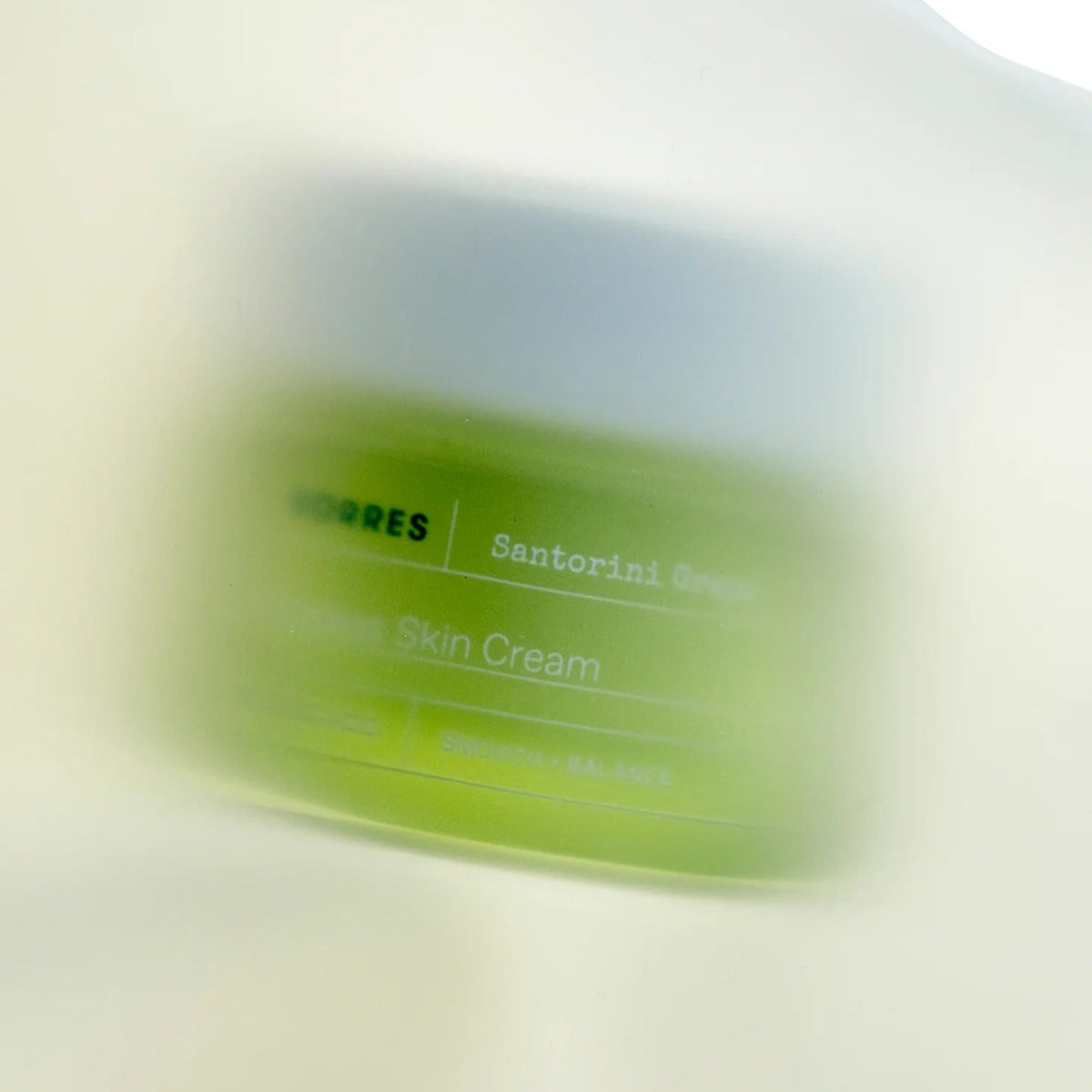 Blurred container of Santorini Green Skin Cream on a light background