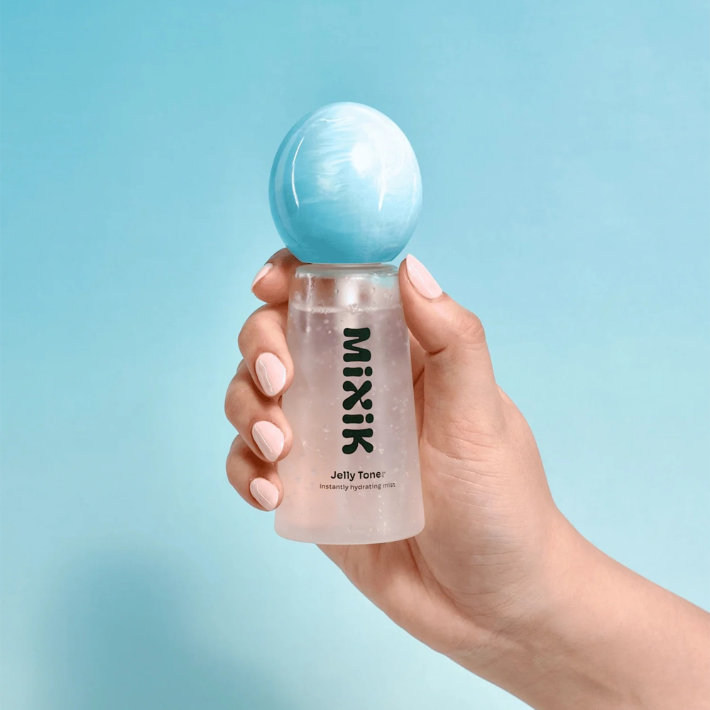 A hand holding a clear cylindrical bottle of MIXIK Jelly Toner with a light blue spherical cap, set against a solid light blue background.