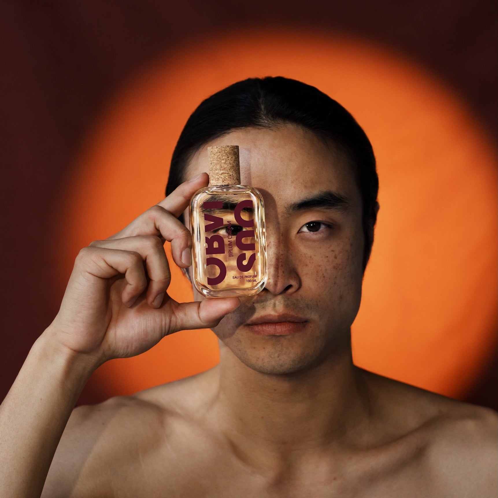 Person holding a bottle of Plum Cream perfume against an orange background