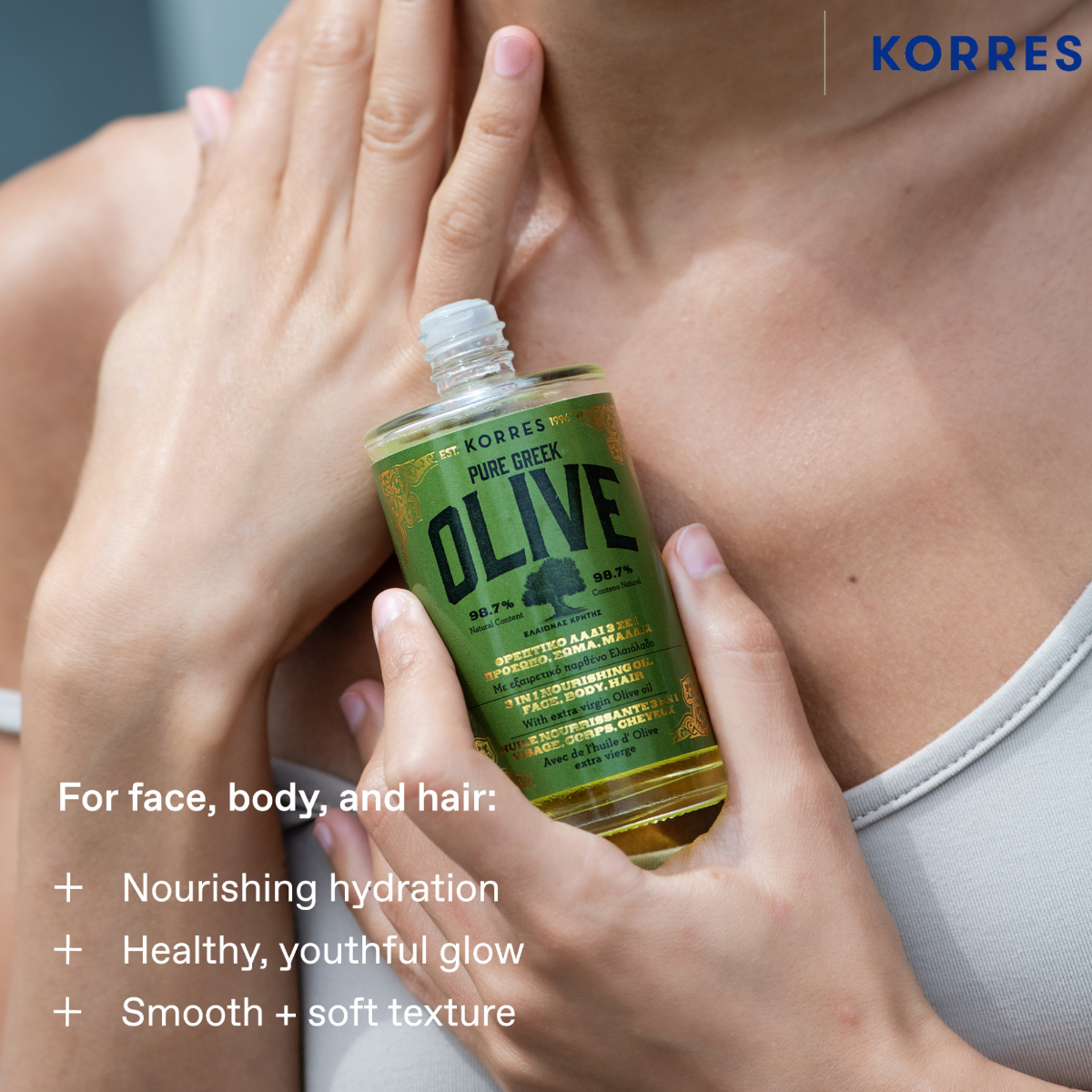 A person holding a bottle of KORRES Pure Greek Olive moisturizing cream against their chest, with text overlays highlighting benefits for face, body, and hair.