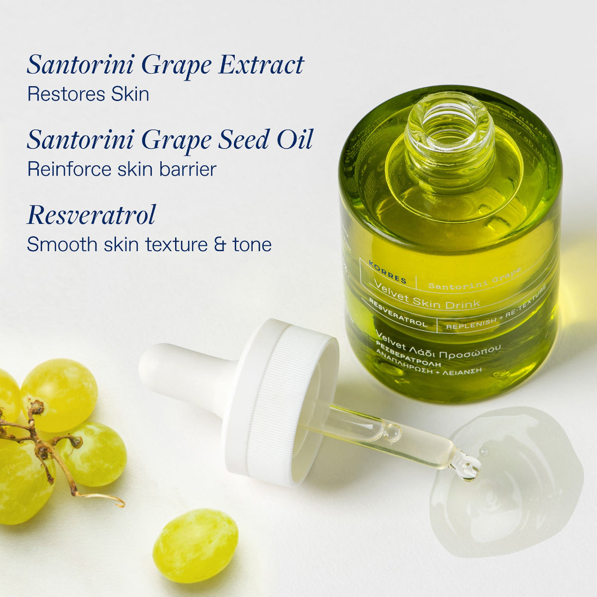 A bottle of Korres Velvet Skin Drink Oil facial serum with a dropper, shown on a white background with text describing benefits and green grapes as props.
