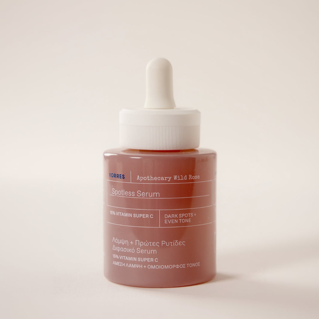 Korres Apothecary Wild Rose Spotless Serum in a glass bottle with a white dropper cap, shown on a warm off-white background.