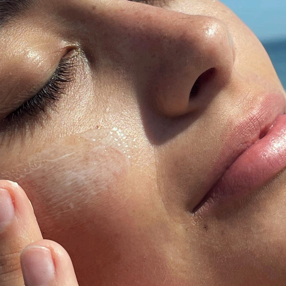 Close-up of a person's face with Korres Santorini Grape Poreless Skin Cream on their cheek.