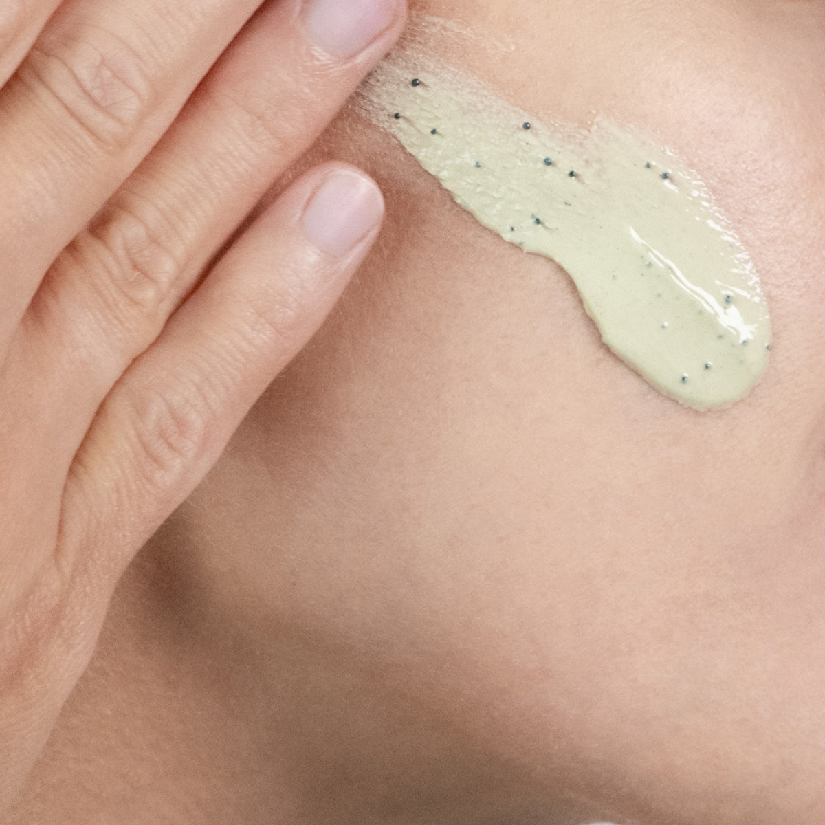 A close-up of a hand applying Santorini Grape Volcanic SkinReset Mask onto a person's face.