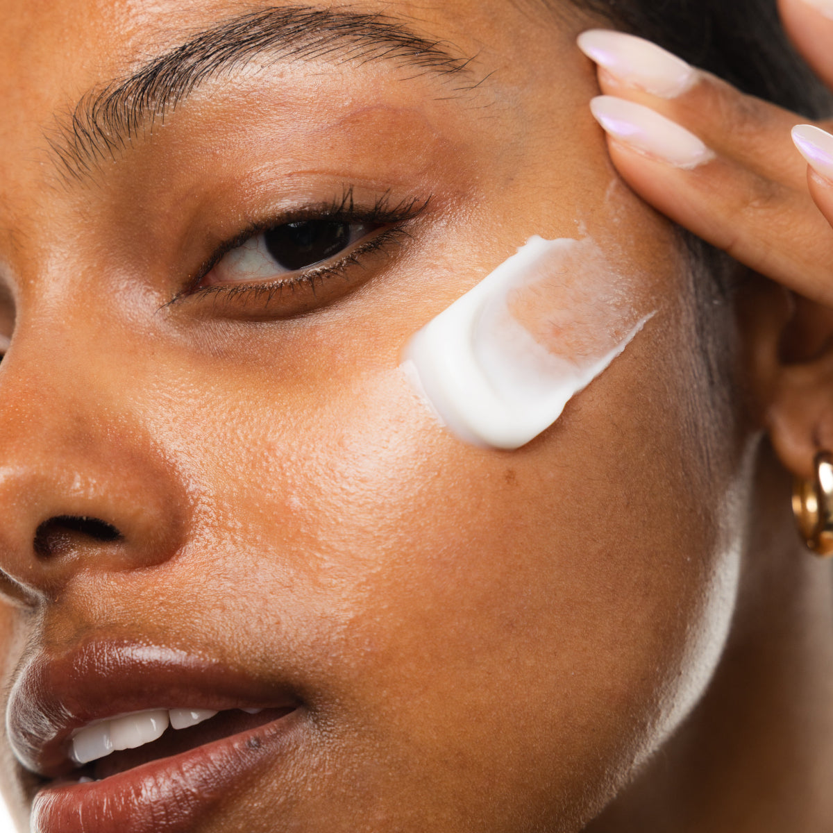 Woman applying cream to her face with a close-up focus on her eye area.