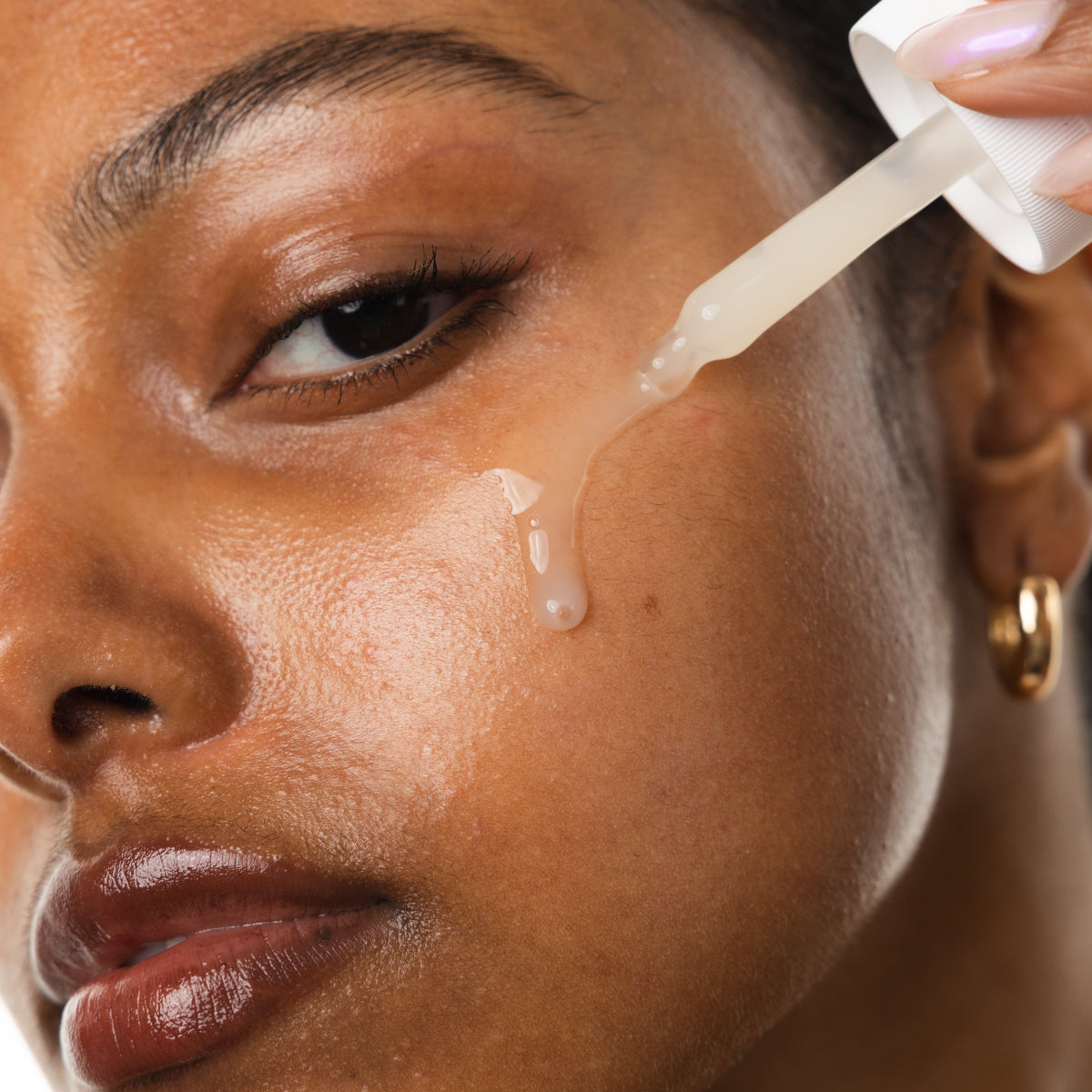 Person applying a dropper of skincare product to their face
