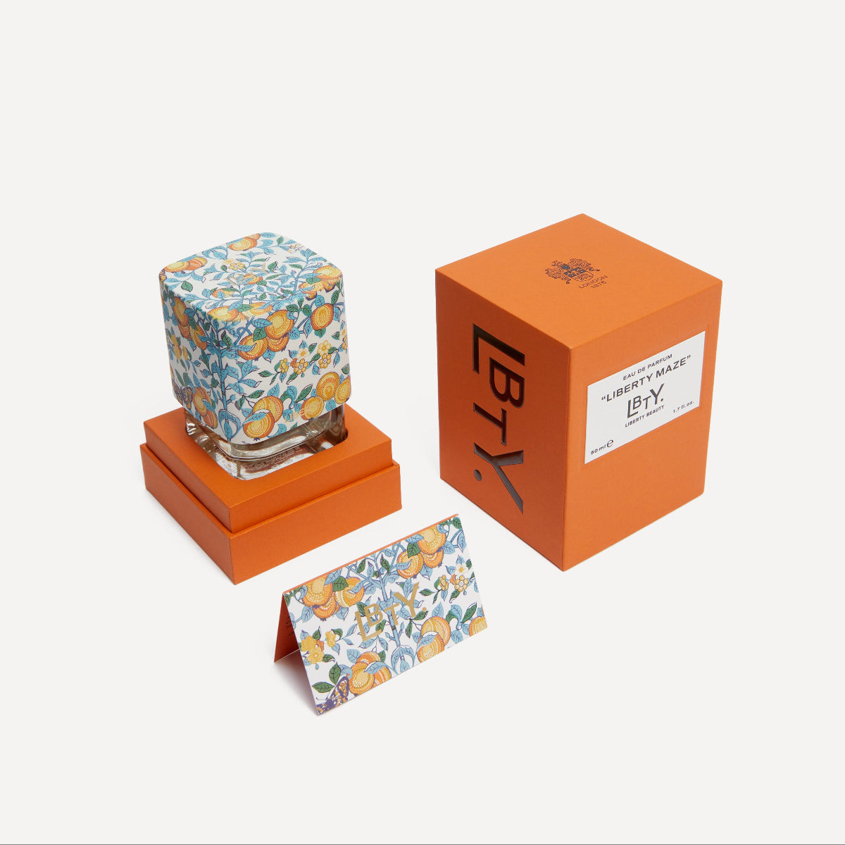 Liberty Maze Eau de Parfum with floral design on an orange stand, next to an orange box with a LBTY label.