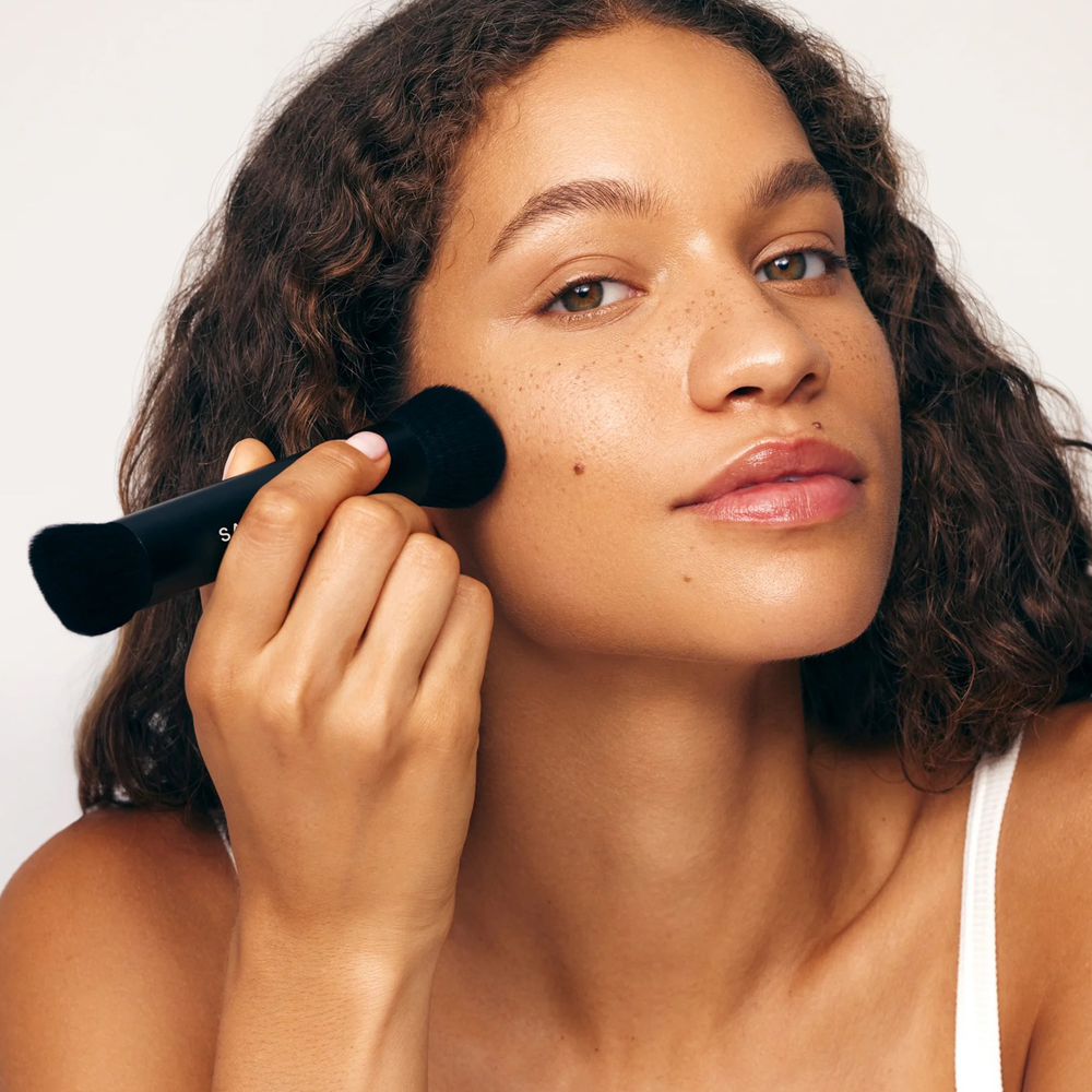 Woman with brush on her face, on a plain background