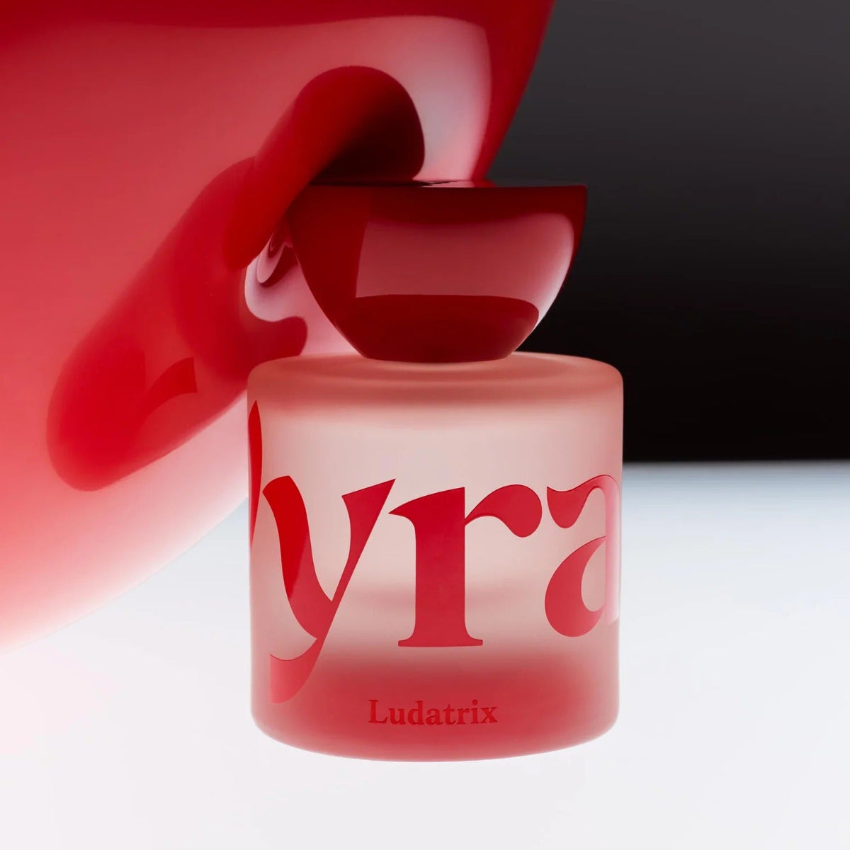 Ludatrix Eau de Parfum bottle on a white surface presse against red latex.