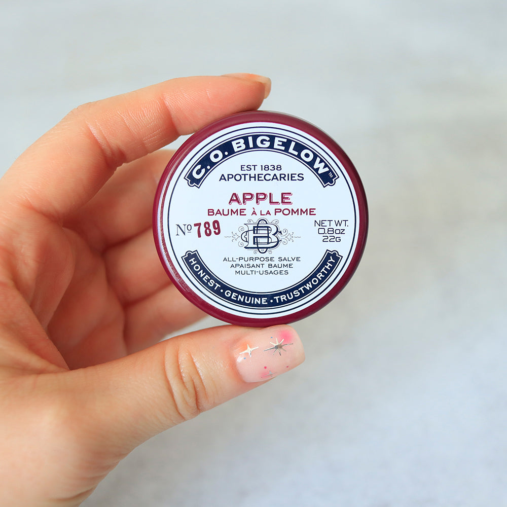 C.O. Bigelow Apple salve container held in a hand against a light background