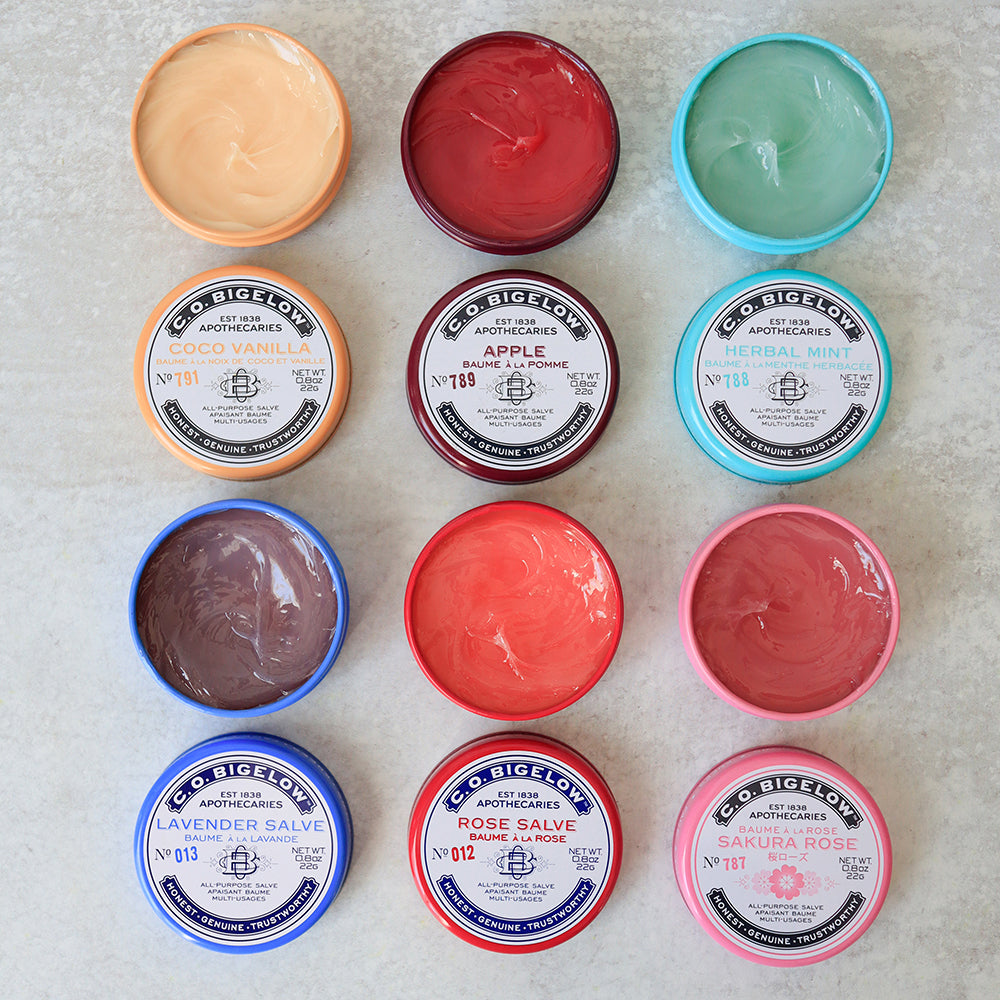 Assorted C.O. Bigelow lip balms in various colors on a textured surface