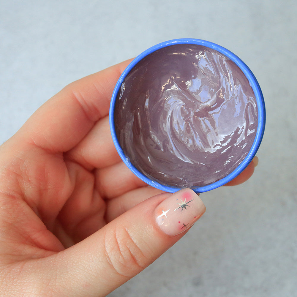 Hand holding C.O. Bigelow Lavender Salve on  a light gray background
