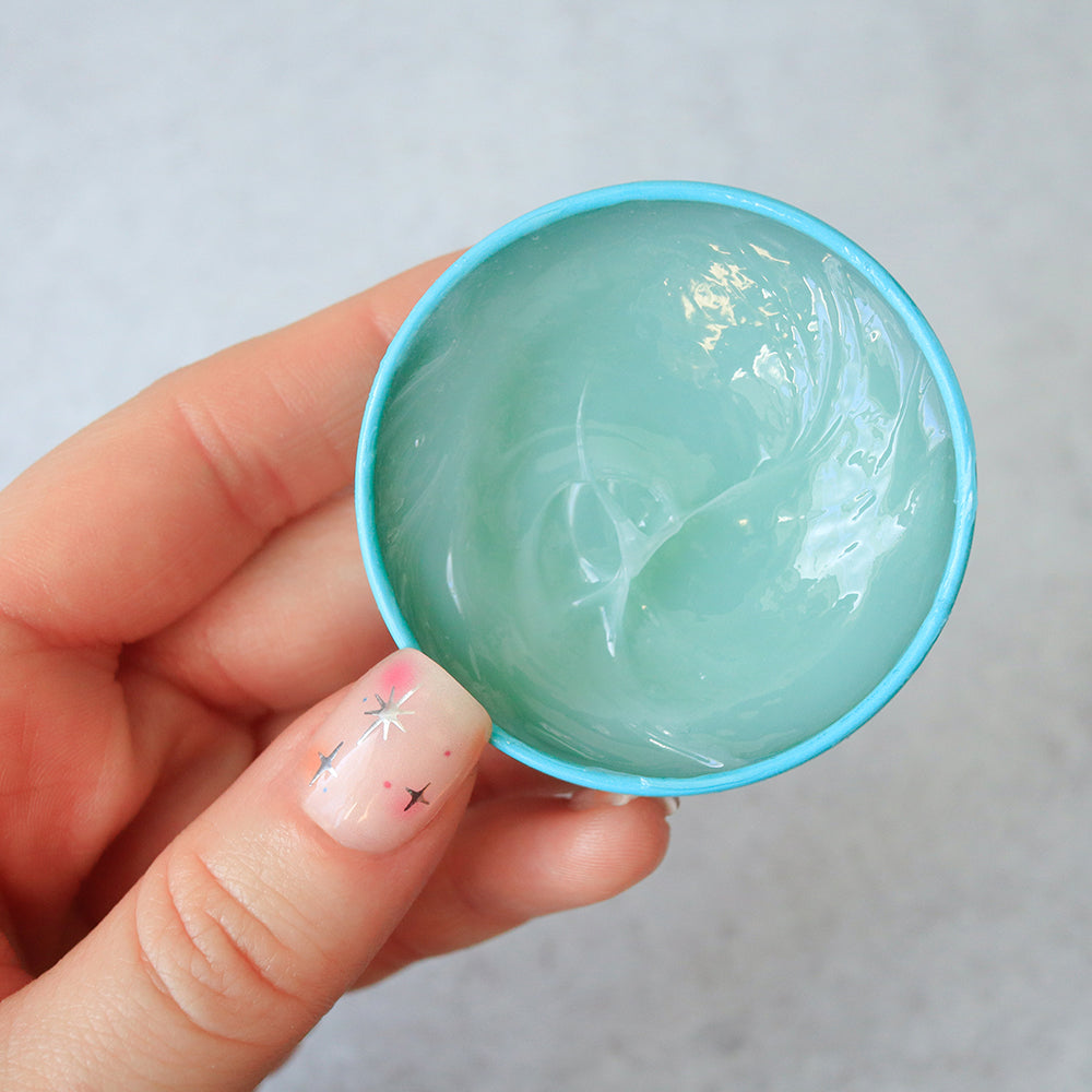 Hand holding C.O. Bigelow Herbal Mint salve container against a light gray background