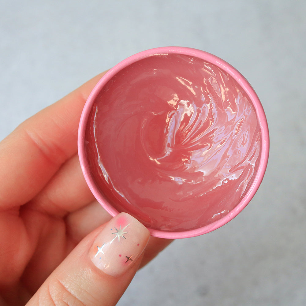 Hand holding a Sakura Rose Salve Tin against a gray background