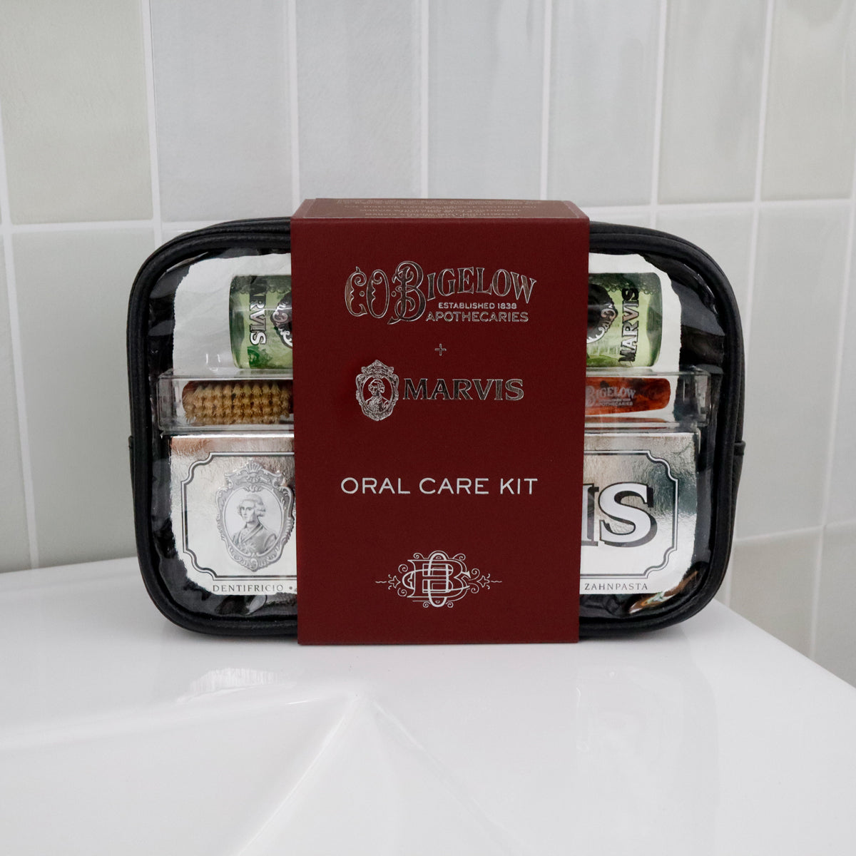 Bigelow x Marvis Oral Care Kit in a black zippered case with a prominent dark red box in the center, set on a white surface against a white tiled background.