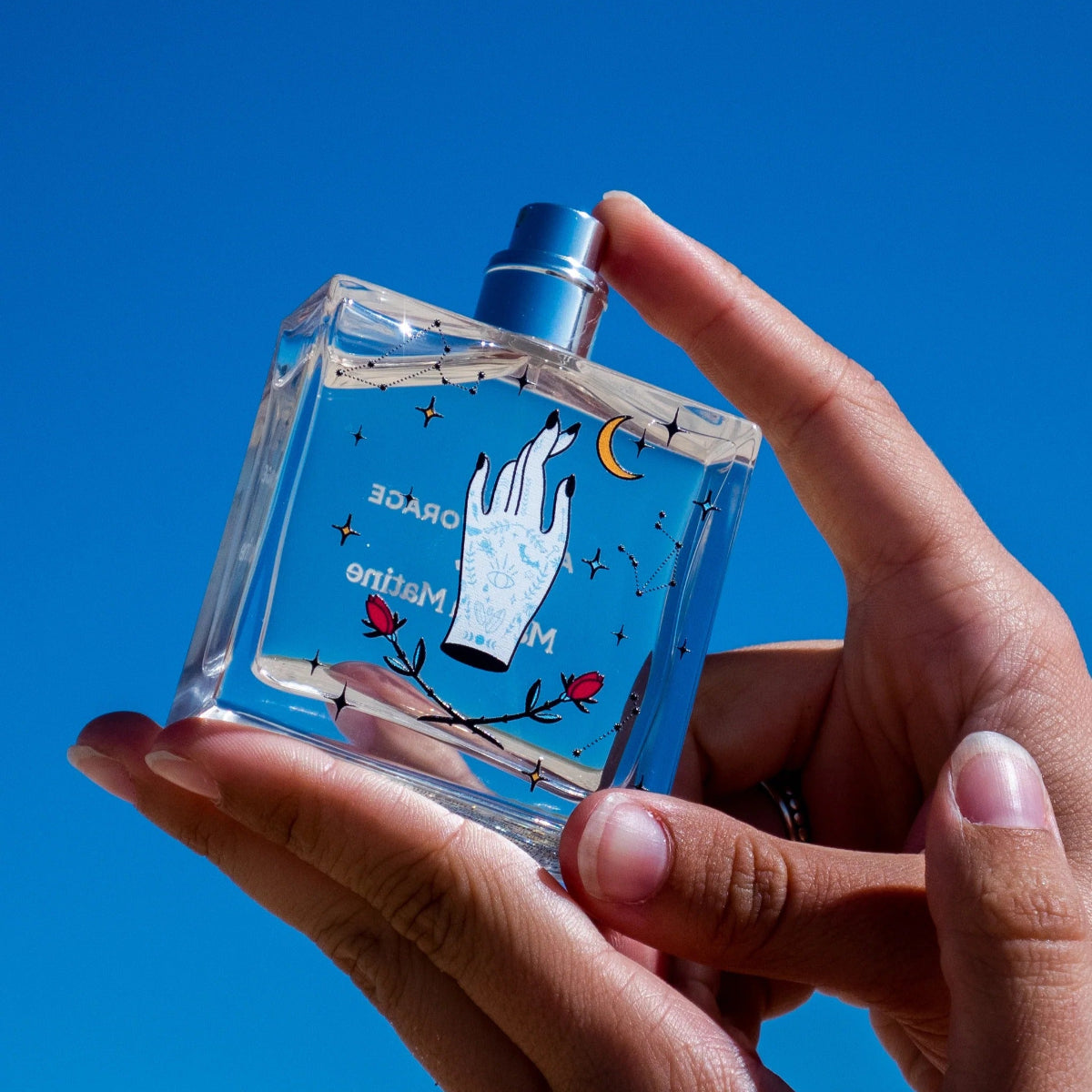 Clear perfume bottle with artistic design held against a blue sky