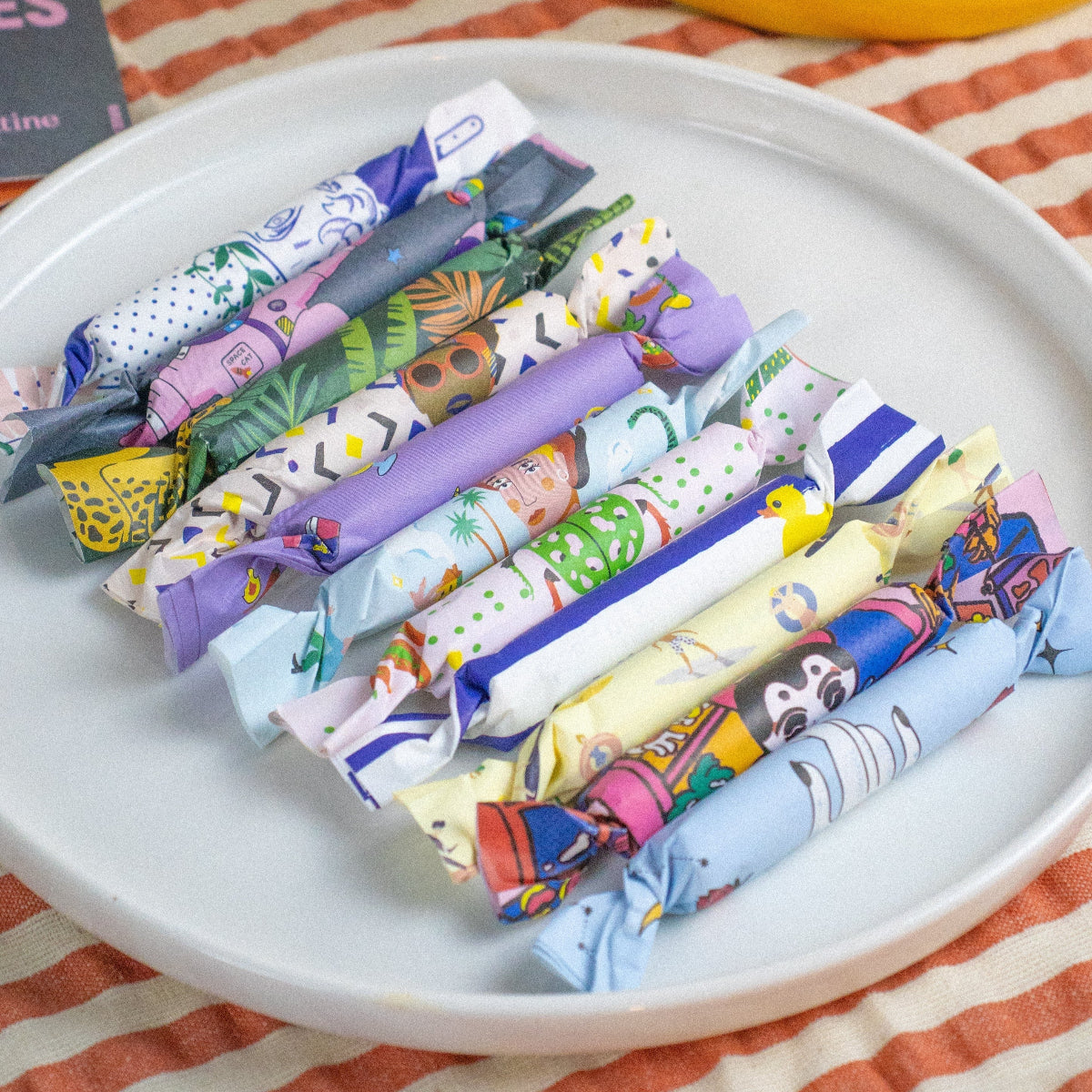 Maison Matine Mini Perfume Samples in colorful paper rolls on a white plate with a striped tablecloth background