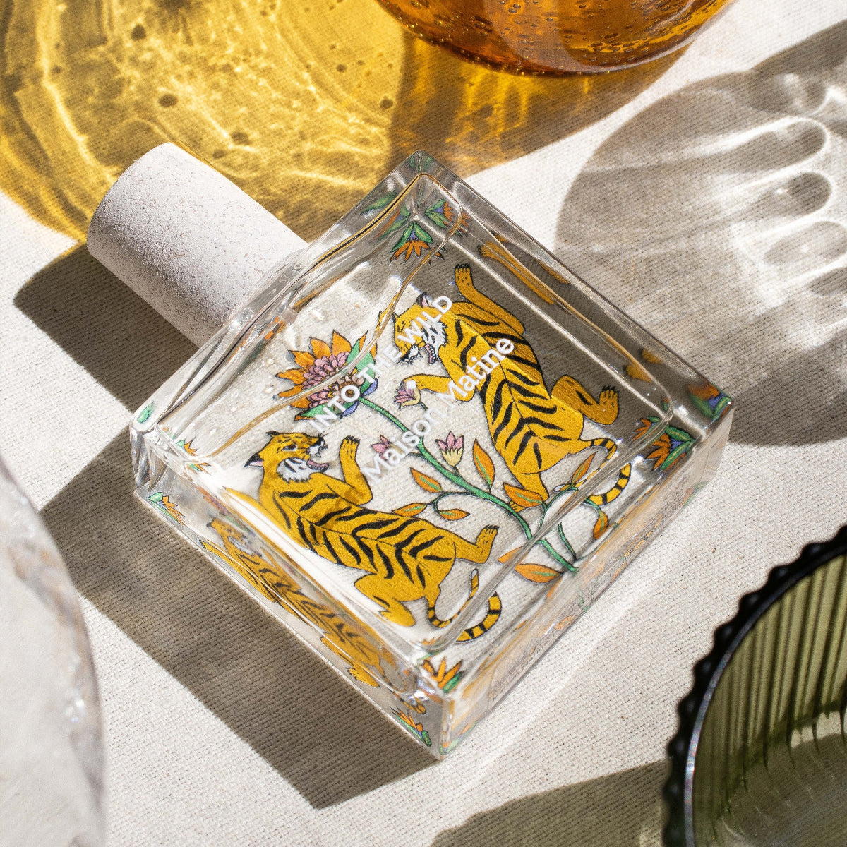 Decorative glass bottle with tiger design on a white surface with amber glass item in the background