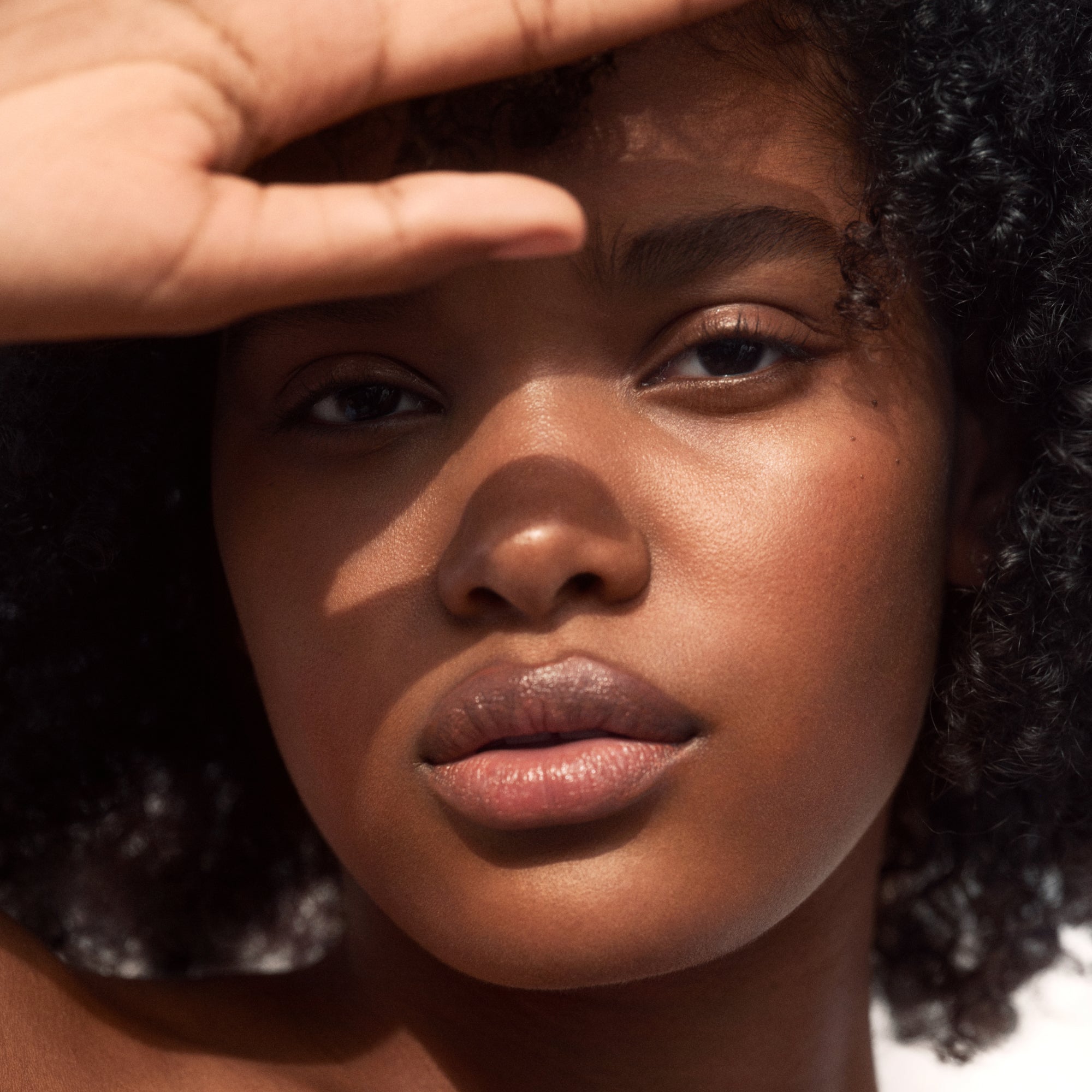 Close-up of a person shielding their eyes from the sun with a hand.