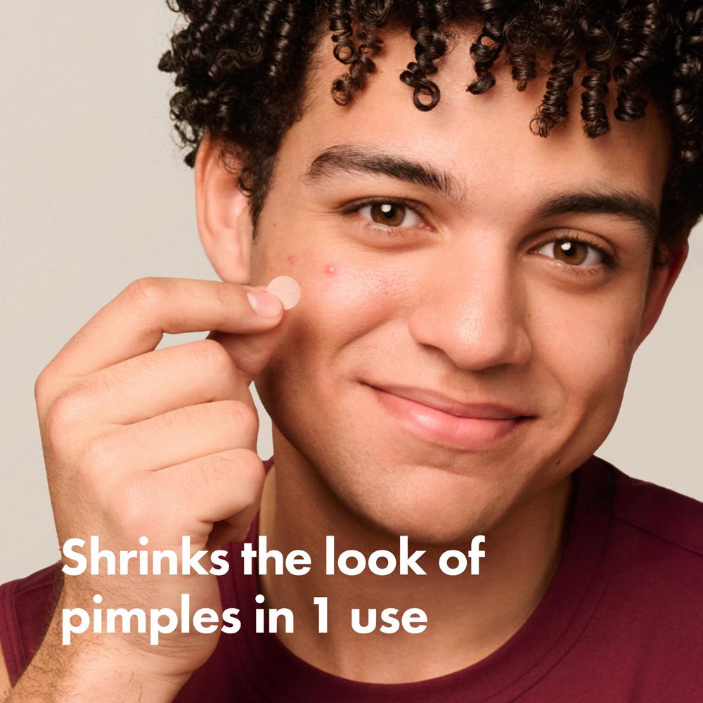 Person holding product with text 'Shrinks the look of pimples in 1 use' on a plain background