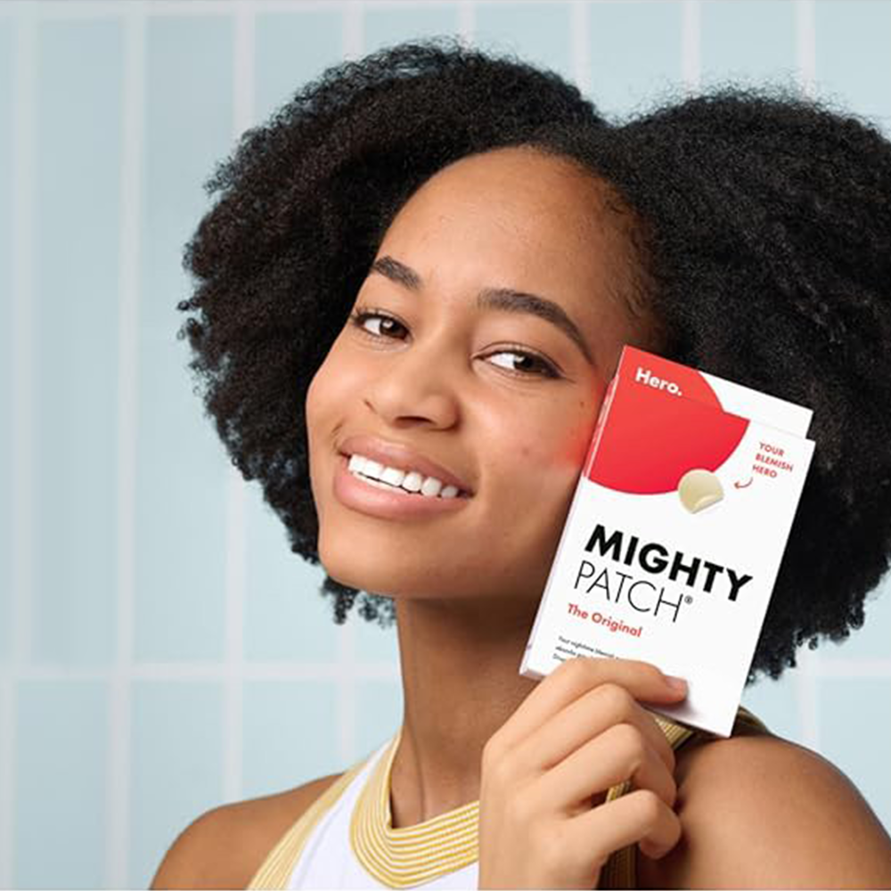 Woman holding a box of Mighty Patch against a tiled wall background