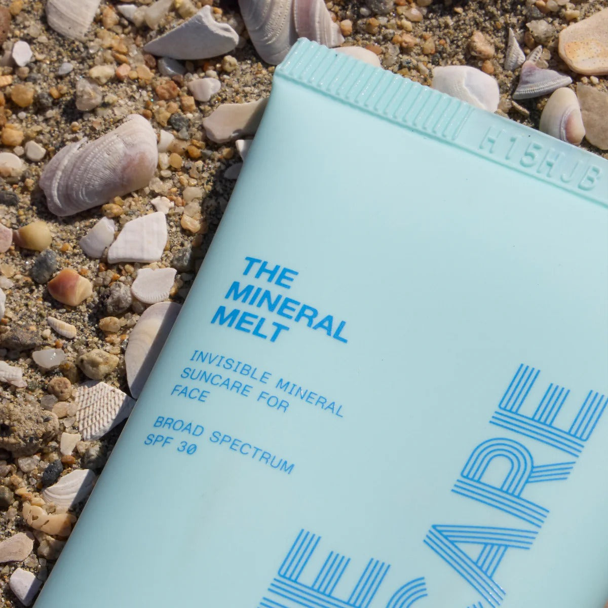 Light blue sunscreen tube labeled 'The Mineral Melt' on a sandy background with shells.