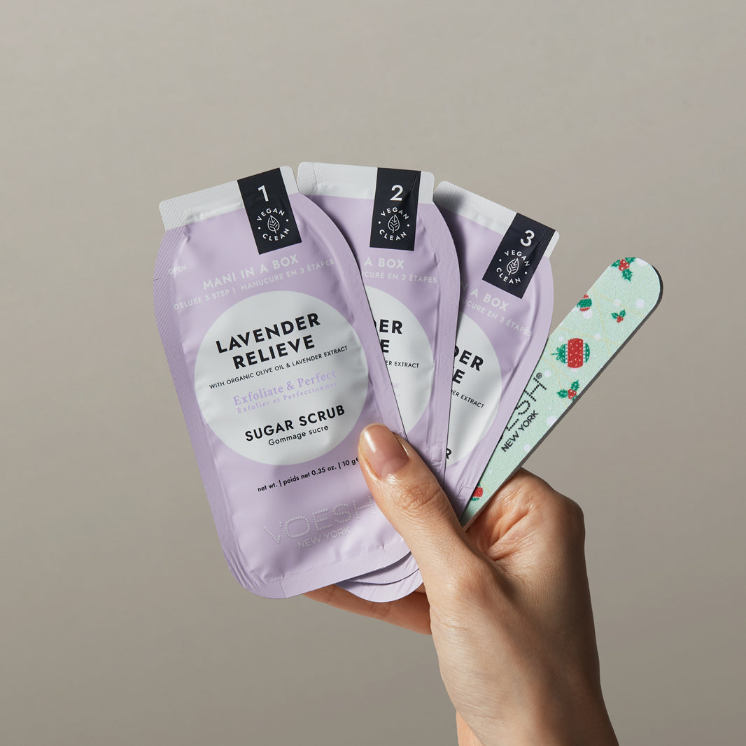 Hand holding multiple packages of Lavender Relieve sugar scrub against a neutral background