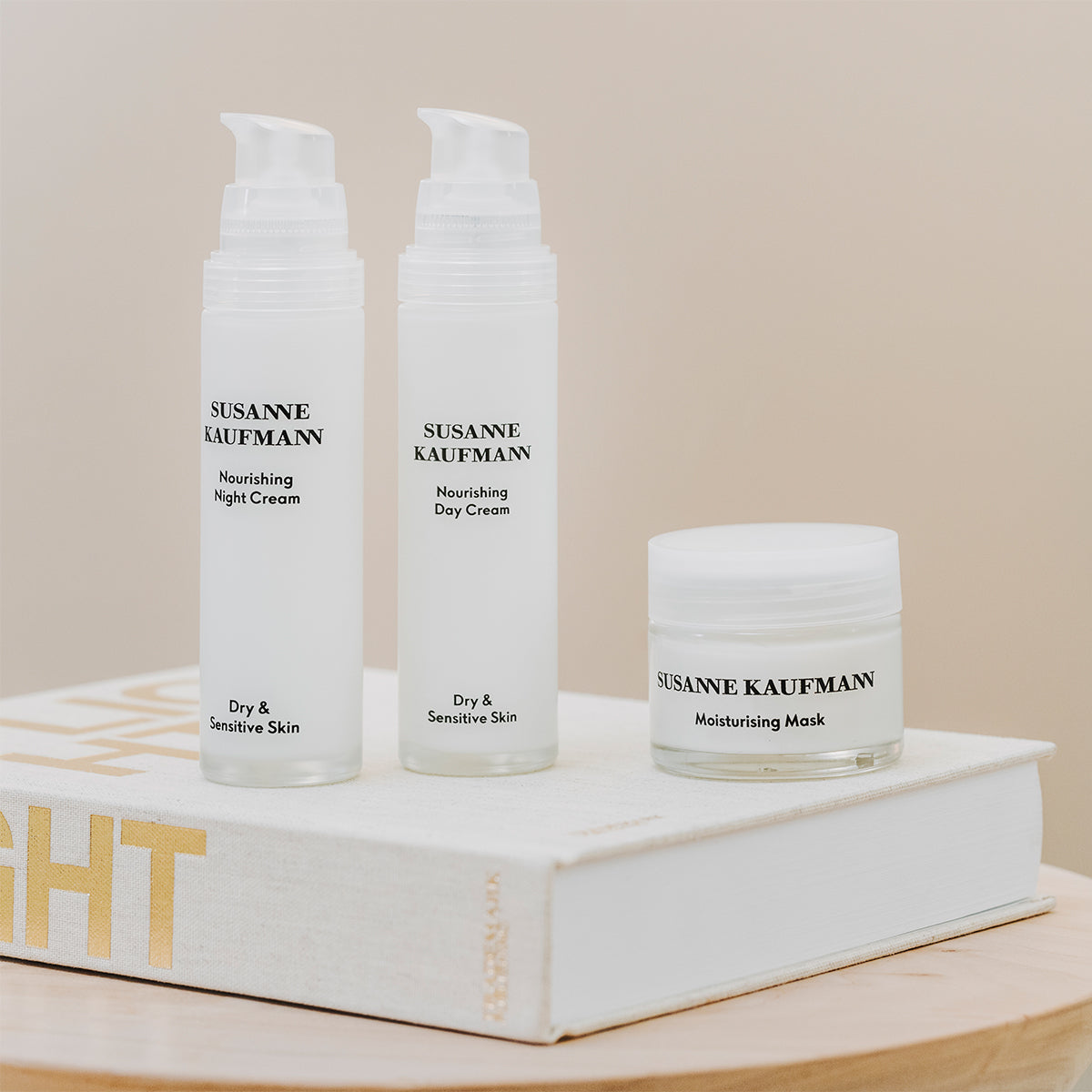 Three Susanne Kaufmann skincare products on a book with a beige background