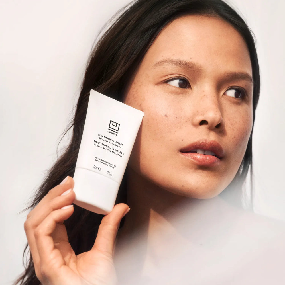 Woman holding a skincare product with a plain background