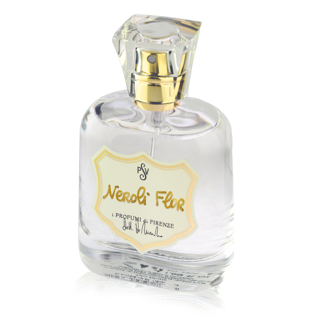 A clear glass perfume bottle with a faceted clear cap and a gold atomizer, featuring a cream-colored shield-shaped label with gold lettering that reads 'Neroli Flor' and 'i Profumi di Firenze'.