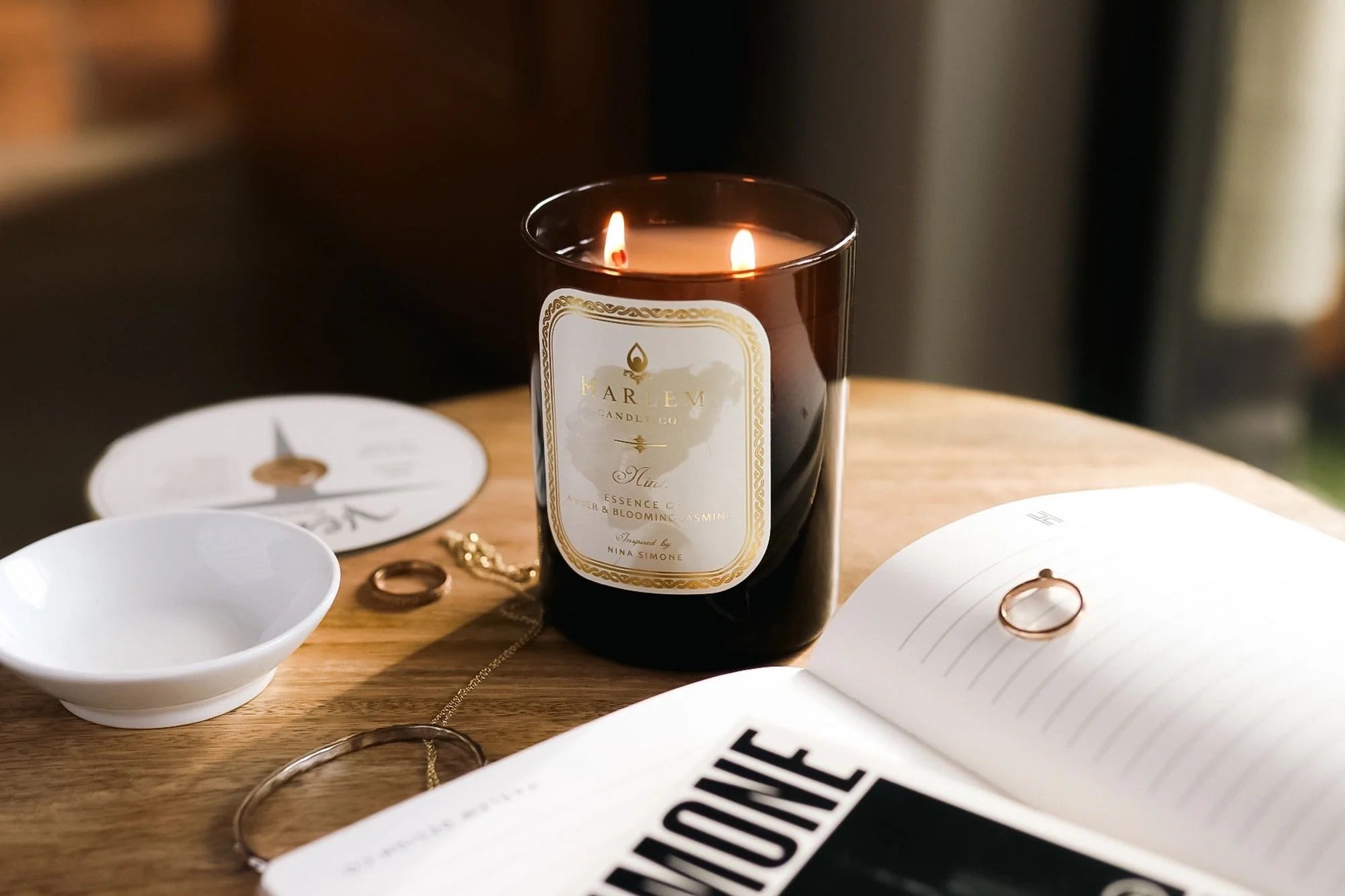 Candle with a label on a table next to a book and jewelry