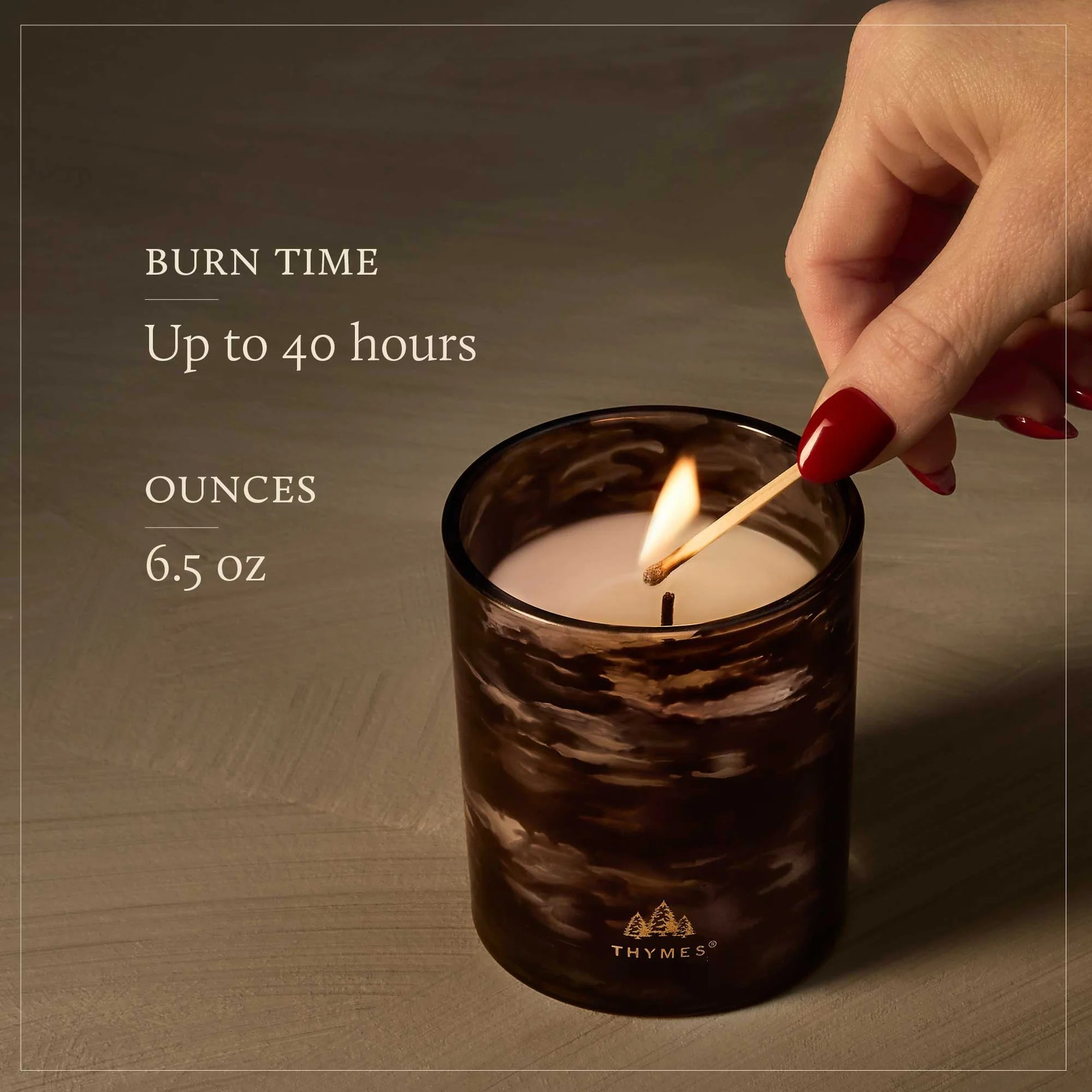 Candle being lit with text about burn time and ounces, on a wooden surface.