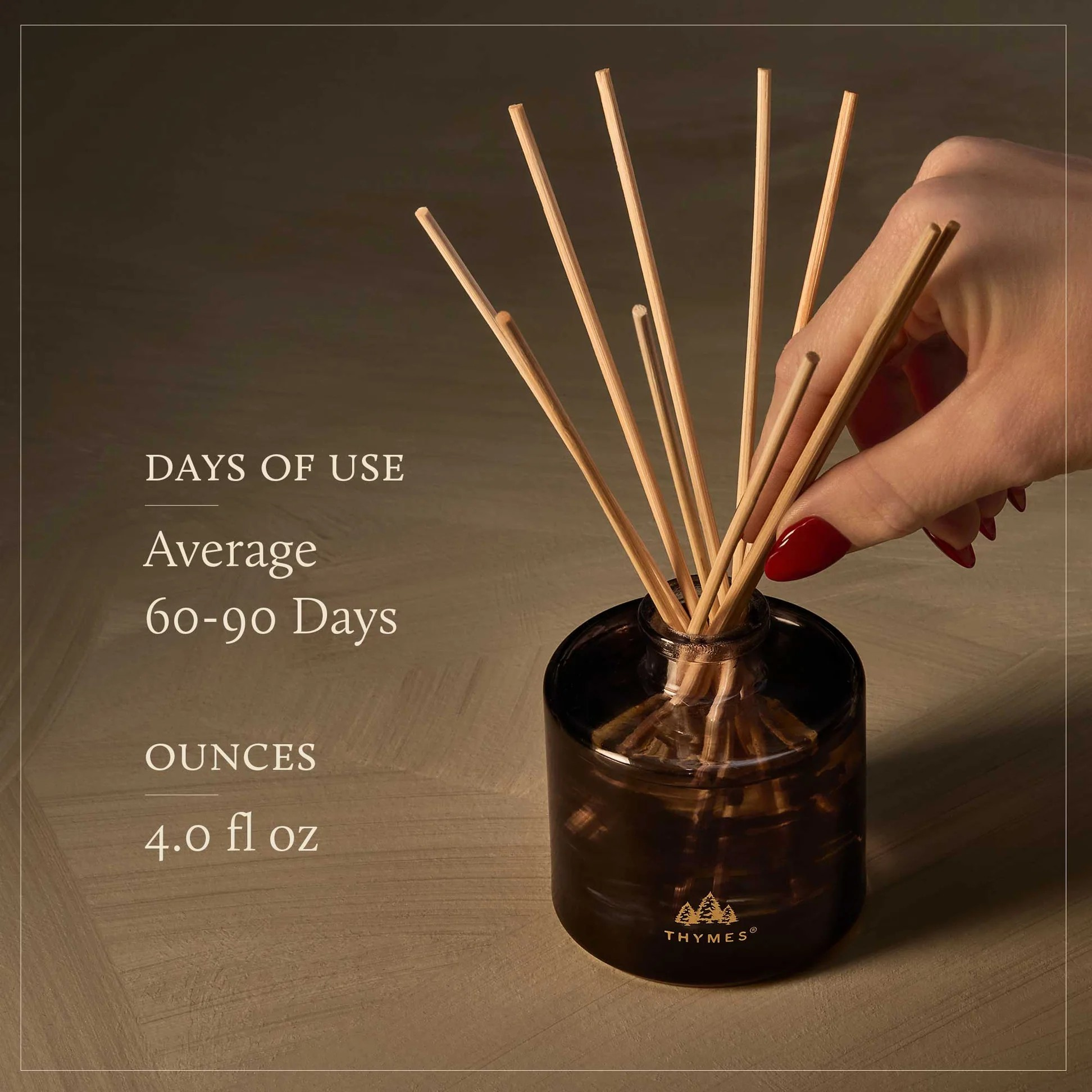 Hand placing reed diffuser sticks into a container with product details on a wooden background