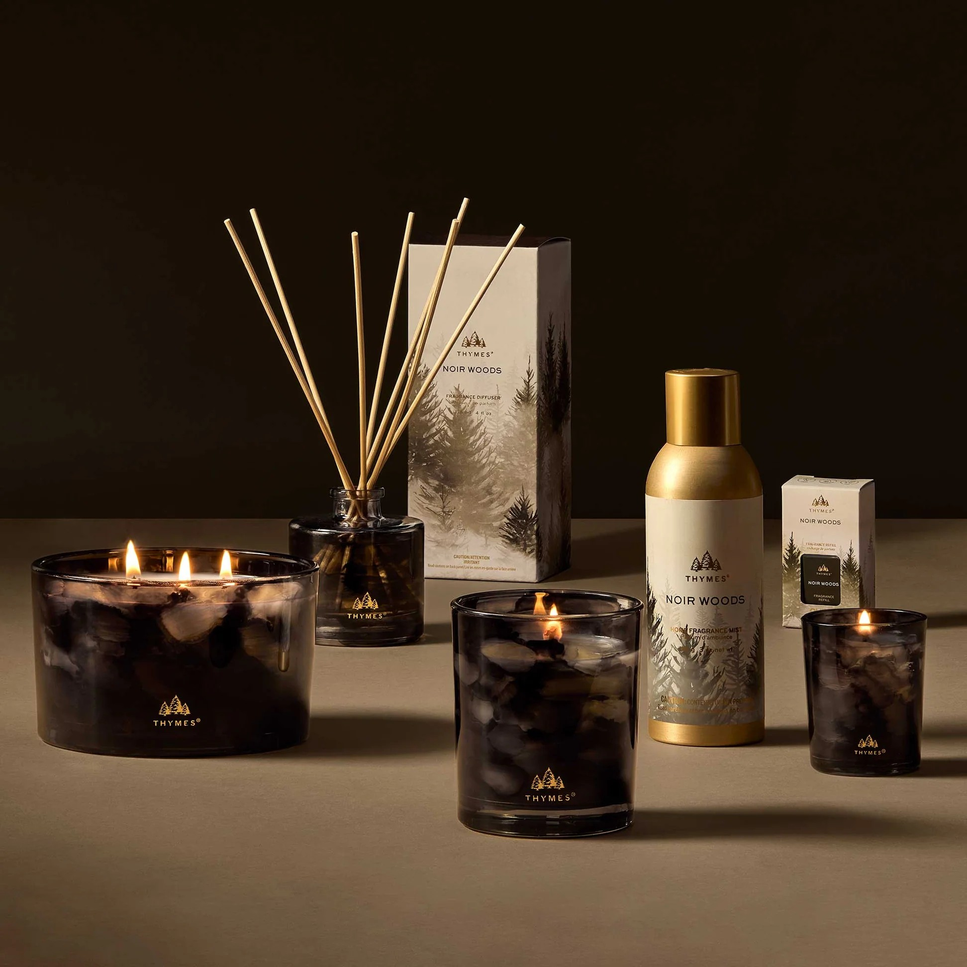 Collection of Thymes Noir Woods products including candles and diffusers on a dark background