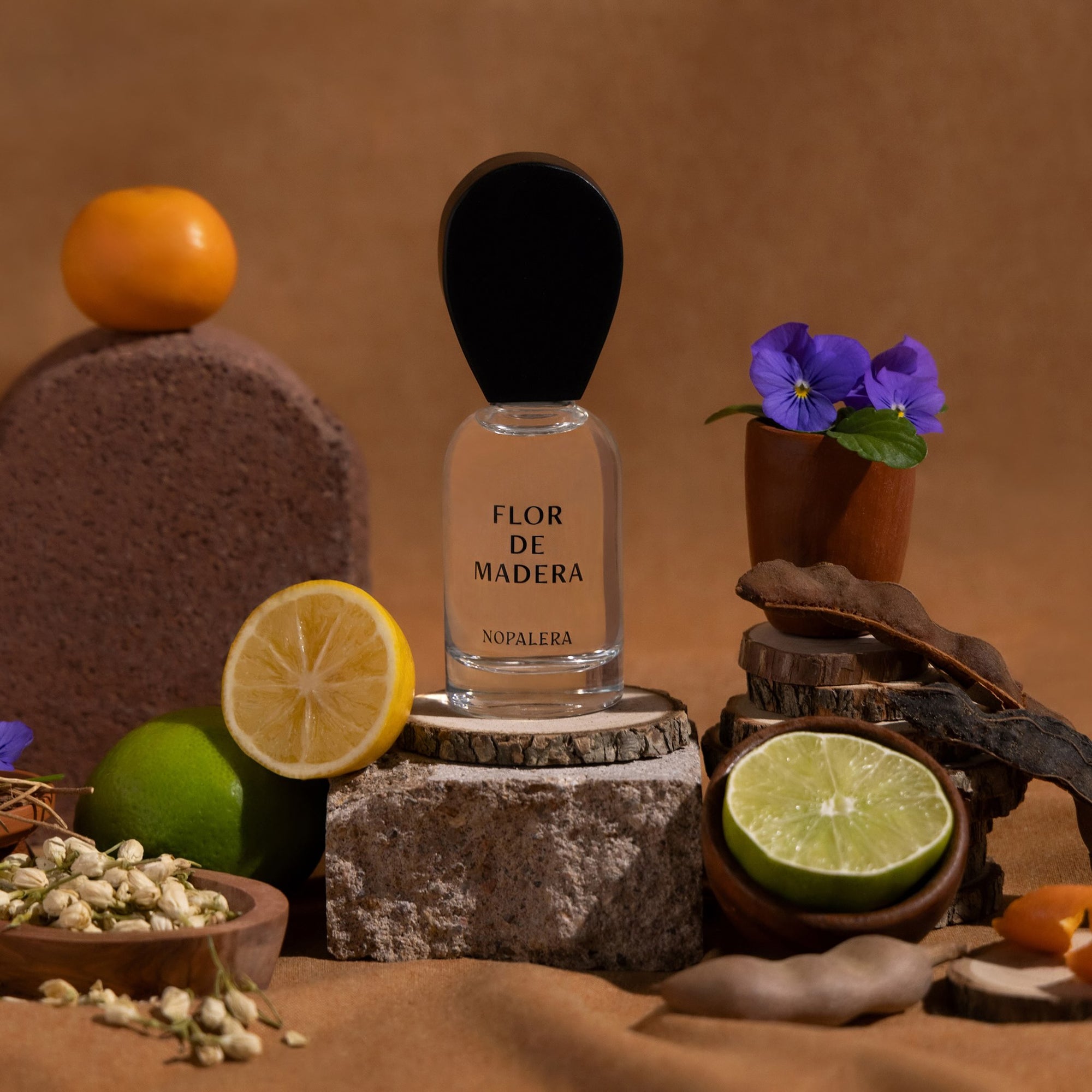 Perfume bottle labeled 'Flor de Madera' surrounded by fruits and flowers on a brown background
