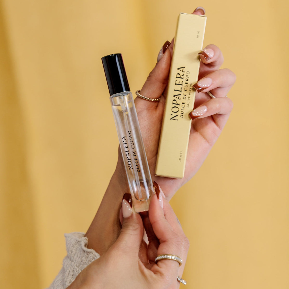 Hands holding a Nopalera perfume bottle and box against a yellow background