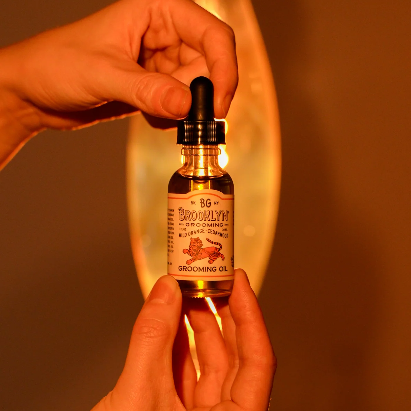 Hand holding a dropper bottle labeled 'Brooklyn' with a warm glow in the background