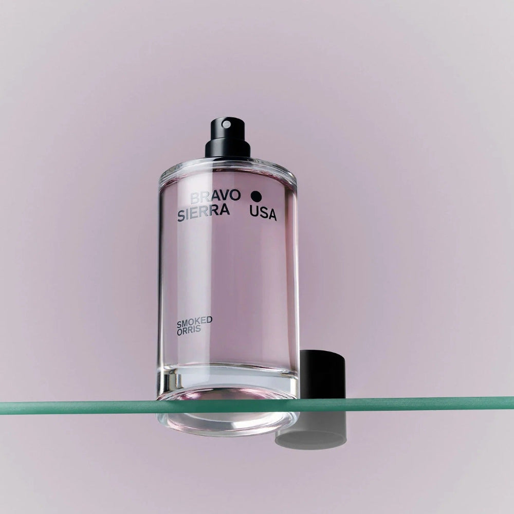 Clear glass bottle with black cap on a glass shelf against a light purple background
