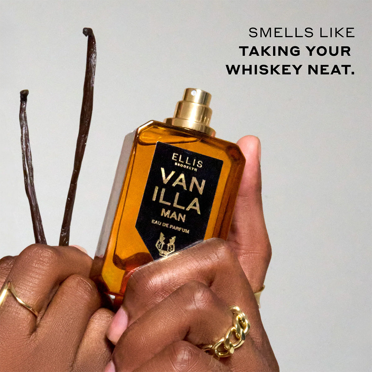 Bottle of Ellis Vanilla Man perfume held by a hand with vanilla beans on a light background